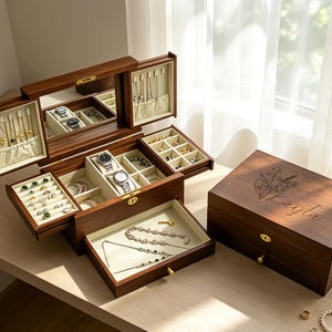 May include: A dark wooden jewellery box with multiple compartments, including a mirror and drawers. The box is open, displaying various jewellery items like rings, bracelets, and necklaces. A closed box with the name "Kayla" is also visible. The wood has a warm, brown tone.