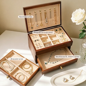 May include: A wooden jewelry box with multiple compartments for necklaces, rings, earrings, bracelets, and other jewelry. The box is open, revealing various pieces of jewelry. The interior is lined with a beige fabric.