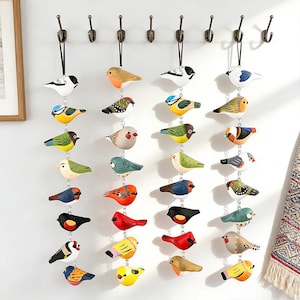 May include: A display of painted wooden bird ornaments suspended from hooks. The birds feature a variety of colours and patterns, including blue, red, yellow, and green. Each bird hangs by a black string, creating a decorative arrangement.