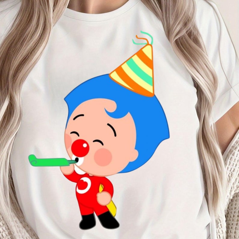 May include: White t-shirt featuring a cartoon character with blue hair, a red nose, and a party hat. The character is wearing a red outfit and blowing a green party horn. The design is centered on the shirt.