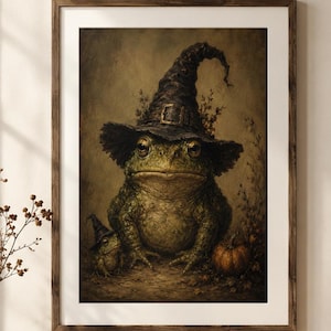 May include: A framed wall art print featuring a large green toad wearing a dark pointed witch hat, accompanied by a smaller toad in a matching hat and a small pumpkin, all set against a dark, textured, earth-toned background.