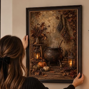 Può includere: Una stampa artistica incorniciata che raffigura una scena scura e suggestiva con un calderone fumante, zucche, fogliame secco e lanterne. L'opera è presentata in una cornice nera, con un'estetica autunnale rustica dai toni marroni e arancioni.