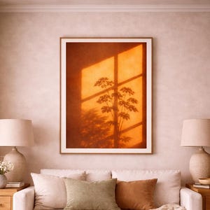 Könnte beinhalten: Wohnzimmer mit einem gerahmten Kunstwerk, das eine Pflanzensilhouette vor orangefarbenem Hintergrund zeigt. Ein weißes Sofa mit Kissen, ein Holztisch und zwei Lampen schaffen eine gemütliche Atmosphäre.