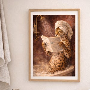 May include: Framed artwork depicts a leopard in a bathtub, wearing a towel on its head and reading a newspaper. The leopard is in a tub with bubbles, under a shower. The artwork is in a bathroom setting with towels, soap dispenser, and toothbrushes.