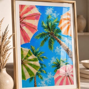 Könnte beinhalten: Ein gerahmtes Gemälde, das einen hellblauen Himmel mit Palmen und vier Strandsonnenschirmen in rosa, weißen, orangefarbenen und grünen Streifen zeigt. Das Kunstwerk weist sichtbare Pinselstriche und eine lebendige Farbpalette auf, gefasst in einem hellen Holzrahmen.