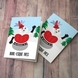 May include: Two greeting cards with a snowman wearing a red heart and a hat with feathers. The text on the cards reads "Burl-Esque Ives".