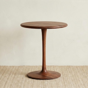 May include: A dark brown, solid wood side table with a round top and base, connected by a slender, curved stem. The table is approximately 24 inches tall and 18 inches wide.