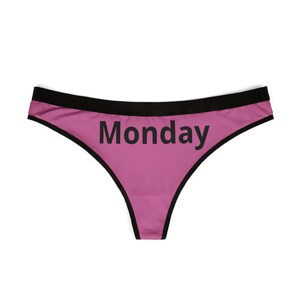 Könnte beinhalten: Rosafarbener String-Tanga mit schwarzem Besatz und dem Wort "Monday" in Schwarz auf der Vorderseite aufgedruckt. Die Unterwäsche ist aus weichem Material und hat einen tiefen Bund.