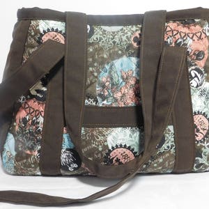 May include: A brown canvas tote bag with a patchwork design featuring a variety of colorful patterns and text. The bag has two top handles and a long shoulder strap.