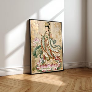 May include: A framed wall art print featuring a figure in traditional robes standing on a large pink lotus flower. The figure wears an ornate golden crown and flowing green and red garments against a textured gold background with lotus leaves.