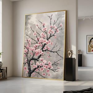 Pode incluir: Uma grande impressão de arte emoldurada em tela com uma cerejeira em flor. A obra apresenta um fundo cinza e branco, um tronco e galhos pretos e flores rosa. A moldura é dourada.