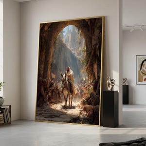 May include: Large framed artwork depicting a biblical scene. A figure in white robes rides a donkey through an archway, surrounded by a crowd. The artwork has a gold frame and is displayed in a modern interior.