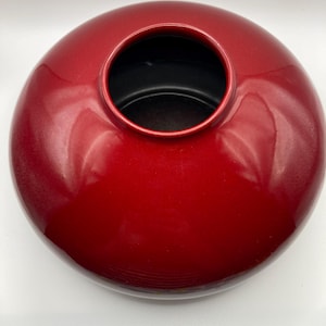 May include: A glossy, round, red vase with a circular opening at the top. The interior of the vase is black. The vase has a smooth, reflective surface.