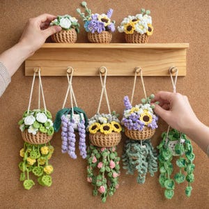 May include: Crocheted hanging basket planters with various colorful flower designs, including white, purple, and yellow blooms. The planters are displayed on a wooden shelf and hanging from a wall, showcasing a handmade craft aesthetic.