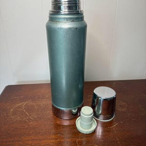 Puede incluir: Un termo vintage azul y plateado con una tapa extra&iacute;ble y un tap&oacute;n separado. El termo tiene una superficie texturizada y una banda plateada alrededor de la parte inferior.