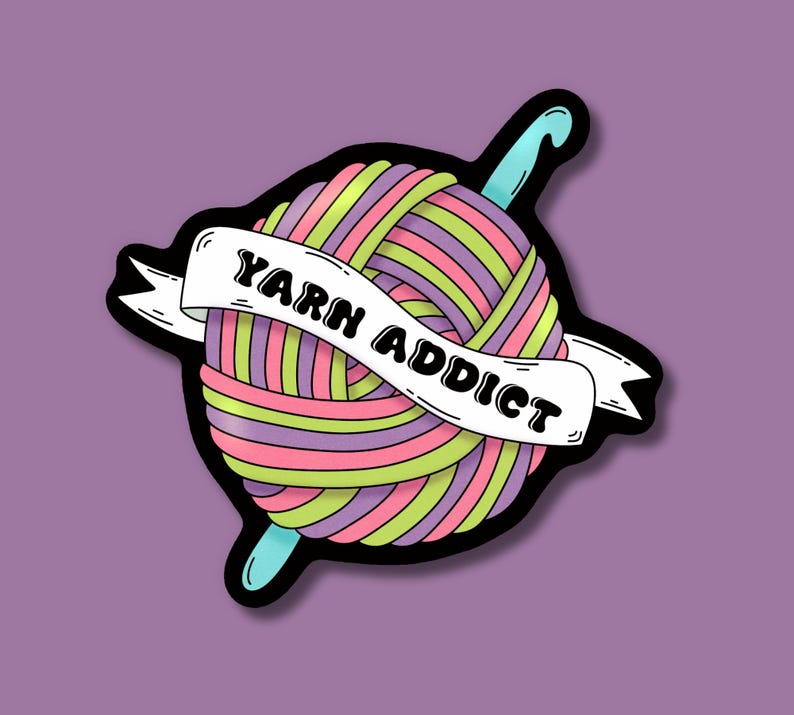 Pode incluir: Um autocolante colorido com uma bola de l&atilde; e uma agulha de croch&ecirc;. A l&atilde; &eacute; listrada com rosa, verde e roxo. Uma faixa branca que atravessa a l&atilde; diz "YARN ADDICT" em texto preto. O autocolante tem um contorno preto sobre um fundo roxo.