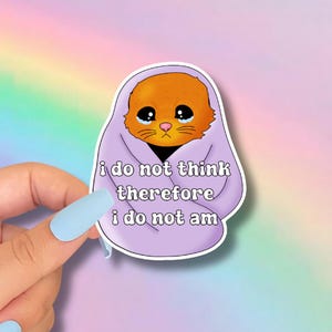 May include: A sticker featuring a cartoon cat wrapped in a purple blanket. The orange cat has large, sad eyes and a yellow nose. The sticker has the text "i do not think therefore i do not am".