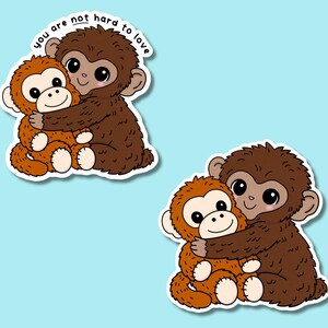 May include: Two stickers featuring cartoon monkeys hugging. One monkey is brown, the other is orange. The text "you are not hard to love" is above the monkeys. The stickers are on a light blue background.