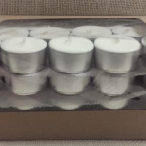 May include: A box of white tea lights in a clear plastic container. The tea lights are arranged in rows and are ready to be used.
