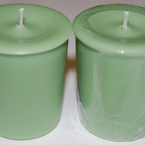 May include: Two light green votive candles with white wicks. One candle is unwrapped, and the other is wrapped in clear plastic. The candles have a cylindrical shape with a slightly wider top.