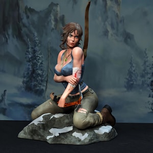 May include: A detailed figurine of a woman kneeling on a rock, holding a bow and a pickaxe. She wears a blue tank top, green pants, and brown boots. Her arm is bandaged, and she has a serious expression. The background depicts a snowy mountain scene.