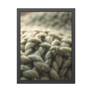 May include: Close-up of a framed image featuring a textured, chunky knit fabric in shades of sage green. The thick yarn is tightly woven, creating a tactile surface. The frame is a simple, dark gray.
