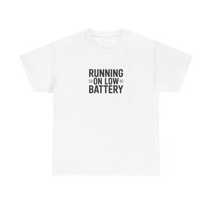 May include: White t-shirt featuring the black text "RUNNING ON LOW BATTERY". The text is in a bold, sans-serif font, with a battery icon. A simple, casual tee, suitable for everyday wear. The design is centered on the chest.