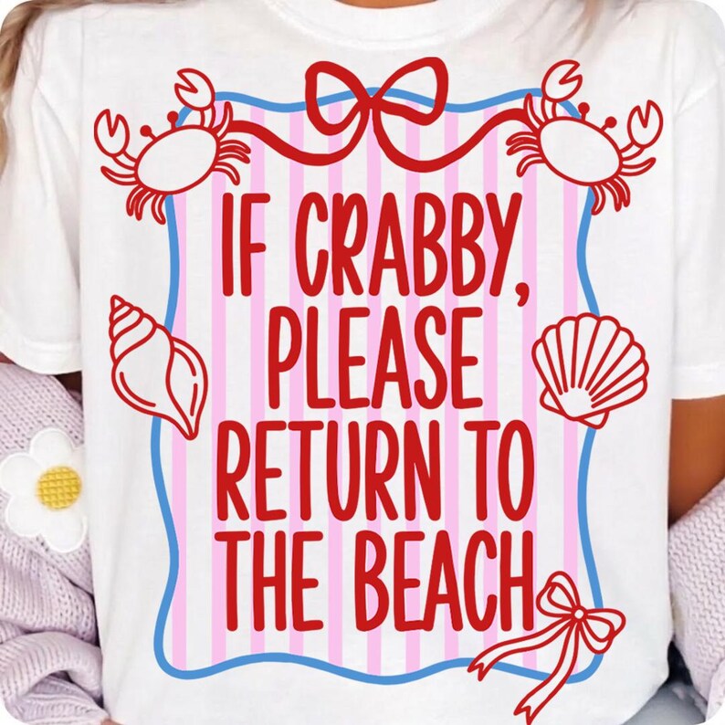 Pu&ograve; includere: T-shirt bianco con un design rosso e blu. La maglietta presenta la scritta "If Crabby, Please Return to the Beach" in rosso, con illustrazioni di granchi, conchiglie e un fiocco. Strisce rosa e bianche sullo sfondo.