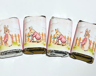 May include: Four wrapped chocolate bars with pink labels featuring a watercolor illustration of a rabbit in a pink coat and a wooden fence. The bars are arranged on a white surface.