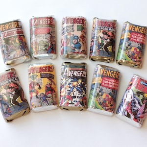 May include: An assortment of cylindrical objects wrapped in comic book covers featuring the Avengers. The covers display various comic book titles with colorful illustrations of superheroes. The objects are arranged on a white surface.