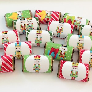 May include: A collection of small chocolate bars wrapped in festive paper featuring illustrations of nutcracker figures. The wrappers display various patterns including red and white stripes, green polka dots, and solid colors with gift graphics.