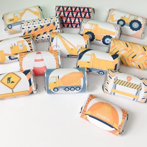 May include: A collection of wrapped candy bars with construction-themed designs. The wrappers feature illustrations of construction vehicles, traffic cones, and warning signs in shades of yellow, orange, blue, and white.