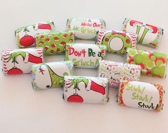 Può includere: Una collezione di dodici incarti rettangolari per caramelle con disegni festivi a tema Grinch in rosso, verde e bianco. Gli incarti mostrano varie illustrazioni di mani verdi, ornamenti rossi e testi tra cui You're A Mean One Mr. Grinch, Don't Be a Grinch e Stink! Stank! Stunk!