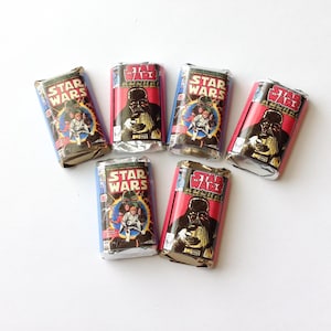 May include: Six candy bars with wrappers designed as vintage Star Wars comic book covers. The wrappers show Darth Vader and other characters, with the Star Wars logo. The wrappers are in red, blue, and silver.