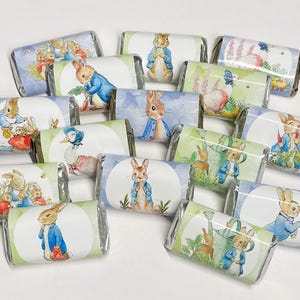 May include: A collection of individually wrapped chocolate bars. Each bar features a different illustration of Peter Rabbit and other characters from the children's book series. The wrappers have a white circle with a pastel background.