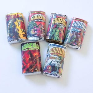 May include: A collection of six vintage Godzilla comic book wrappers. The wrappers feature colorful illustrations of Godzilla and other monsters, with text including "Godzilla King of the Monsters" and "Age of Monsters".