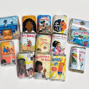 May include: A collection of wrapped chocolate bars with colorful illustrations and text. The bars feature titles like "You Matter," "Ty's Travels," and "Hands Up!" The wrappers showcase diverse characters and themes, suggesting children's literature.