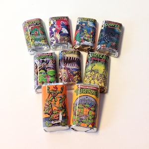 May include: A collection of nine candy bars wrapped in colorful, vintage Teenage Mutant Ninja Turtles themed packaging. The wrappers feature comic book style illustrations of the characters in action, with vibrant colors and bold graphics.