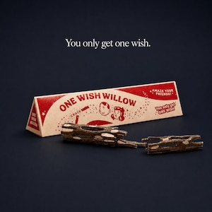 Może przedstawiać: Trójkątne kartonowe pudełko z napisem One Wish Willow w kolorze czerwonym i kremowym, z ilustracjami dwóch twarzy i tekstem You only get one wish. Z przodu leży złamana, teksturowana brązowa gałązka.