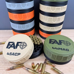 May include: Stacked, multi-colored ammunition storage containers with the text "FAF" and caliber designations. The containers are beige, blue, orange, and olive green. Loose ammunition is scattered around the containers.
