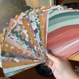 May include: A fan of rectangular cards featuring diverse patterns including floral motifs, abstract wavy lines, and dotted textures in a color palette of mustard yellow, sage green, terracotta, and white, with rounded corners on each individual card.