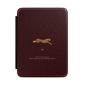 Può includere: Custodia per tablet bordeaux con design di ghepardo dorato. La custodia ha una superficie strutturata e un dorso nero. Il testo "I don't chase I attract. What's meant for me will simply find me" è stampato.