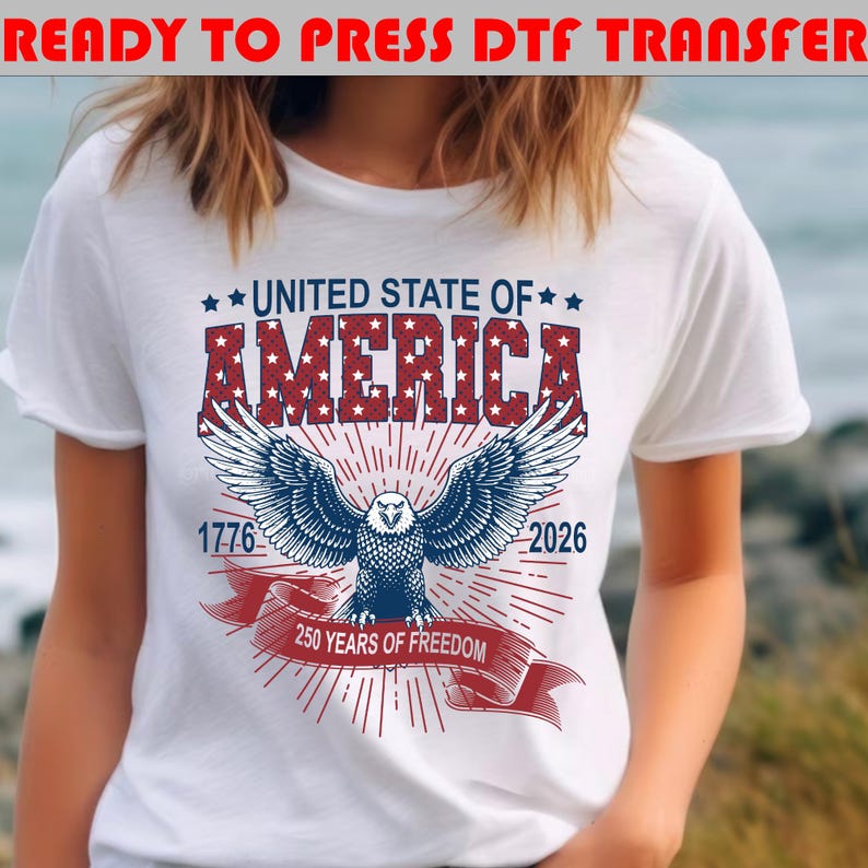 Op de afbeelding: Een wit t-shirt met een afbeelding van een Amerikaanse zeearend met gespreide vleugels, gecentreerd onder de tekst UNITED STATE OF AMERICA. Het ontwerp bevat de jaartallen 1776 en 2026 en een rode banner met de tekst 250 YEARS OF FREEDOM in witte letters.