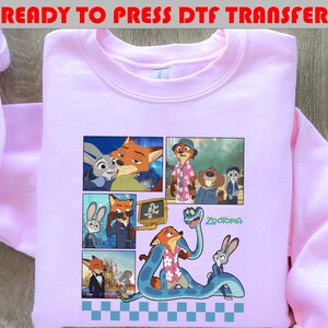 May include: A light pink sweatshirt featuring a colorful graphic of characters from the animated movie "Zootopia." The graphic includes images of a fox, a rabbit, and other characters. Text at the top reads "READY TO PRESS DTF TRANSFER."