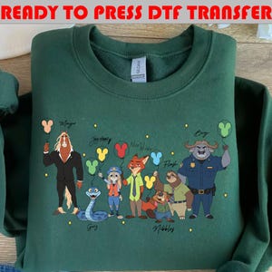 Peut inclure: Un sweat-shirt vert fonc&eacute; avec des personnages de dessins anim&eacute;s de Zootopie, chacun tenant un ballon en forme de Mickey Mouse. Le texte "READY TO PRESS DTF TRANSFER" est en haut. Personnages : Mayor, Judy Hopps, Nick Wilde et Flash.