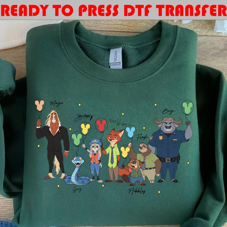 Peut inclure: Un sweat-shirt vert fonc&eacute; avec des personnages de dessins anim&eacute;s de Zootopie, chacun tenant un ballon en forme de Mickey Mouse. Le texte "READY TO PRESS DTF TRANSFER" est en haut. Personnages : Mayor, Judy Hopps, Nick Wilde et Flash.