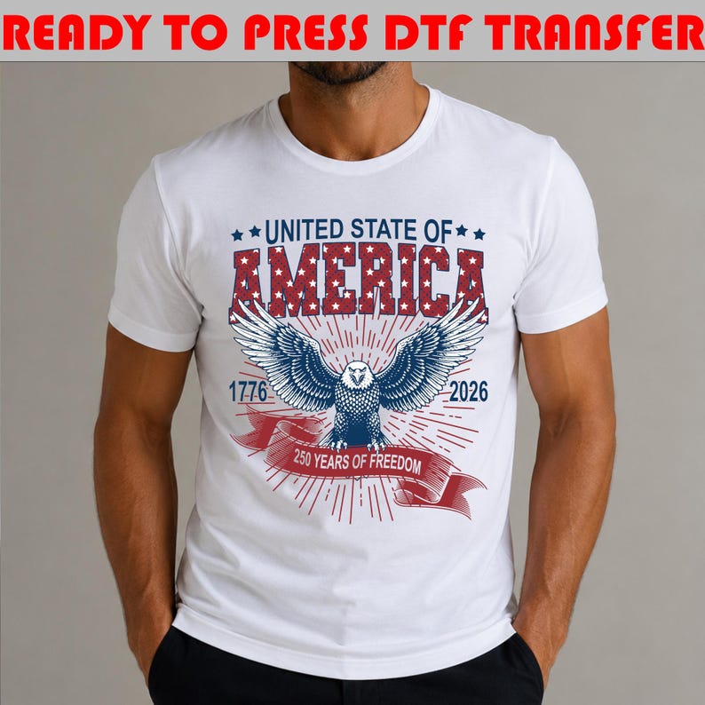 Op de afbeelding: Een wit t-shirt met een afbeelding van een Amerikaanse zeearend met gespreide vleugels, gecentreerd onder de tekst UNITED STATE OF AMERICA. Het ontwerp bevat de jaartallen 1776 en 2026 en een rode banner met de tekst 250 YEARS OF FREEDOM in witte letters.