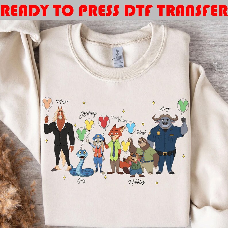 Peut inclure: Sweat-shirt cr&egrave;me avec un motif de personnages de dessins anim&eacute;s tenant des ballons. Les personnages incluent un cheval, un lapin, un renard, un paresseux et un buffle. Le texte en haut indique "READY TO PRESS DTF TRANSFER."