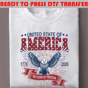 Op de afbeelding: Een wit t-shirt met een afbeelding van een Amerikaanse zeearend, rode en blauwe tekst met UNITED STATE OF AMERICA, 1776, 2026 en 250 YEARS OF FREEDOM. De adelaar staat centraal met gespreide vleugels, omringd door rode zonnestralen en sterren.