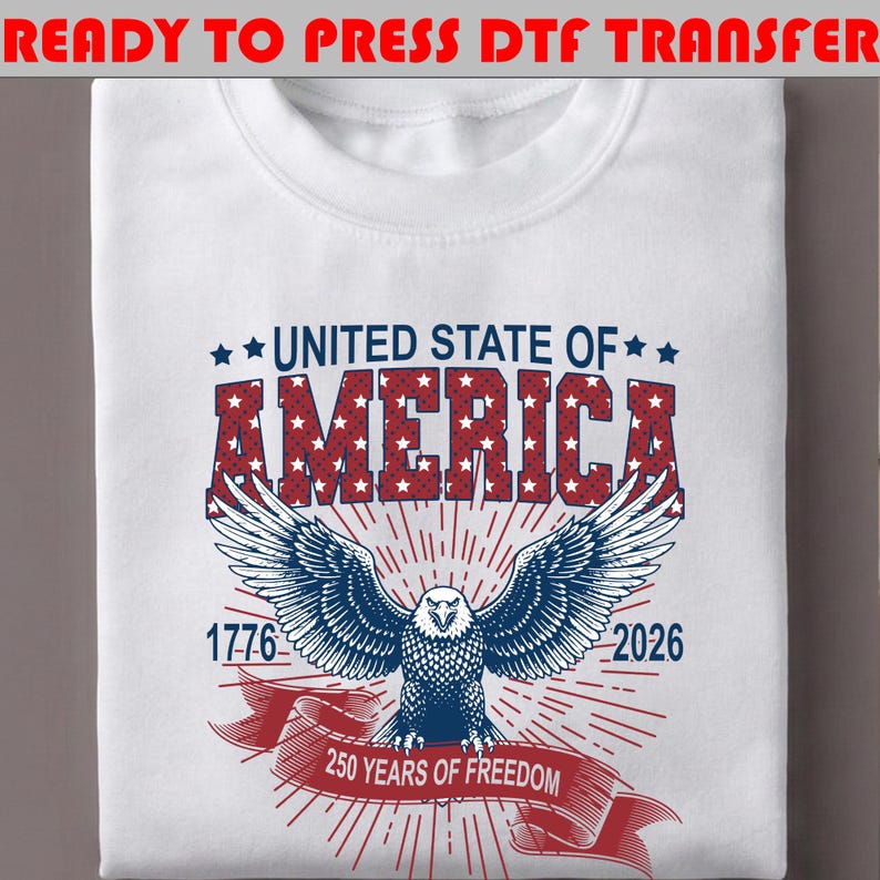 Op de afbeelding: Een wit t-shirt met een afbeelding van een Amerikaanse zeearend, rode en blauwe tekst met UNITED STATE OF AMERICA, 1776, 2026 en 250 YEARS OF FREEDOM. De adelaar staat centraal met gespreide vleugels, omringd door rode zonnestralen en sterren.